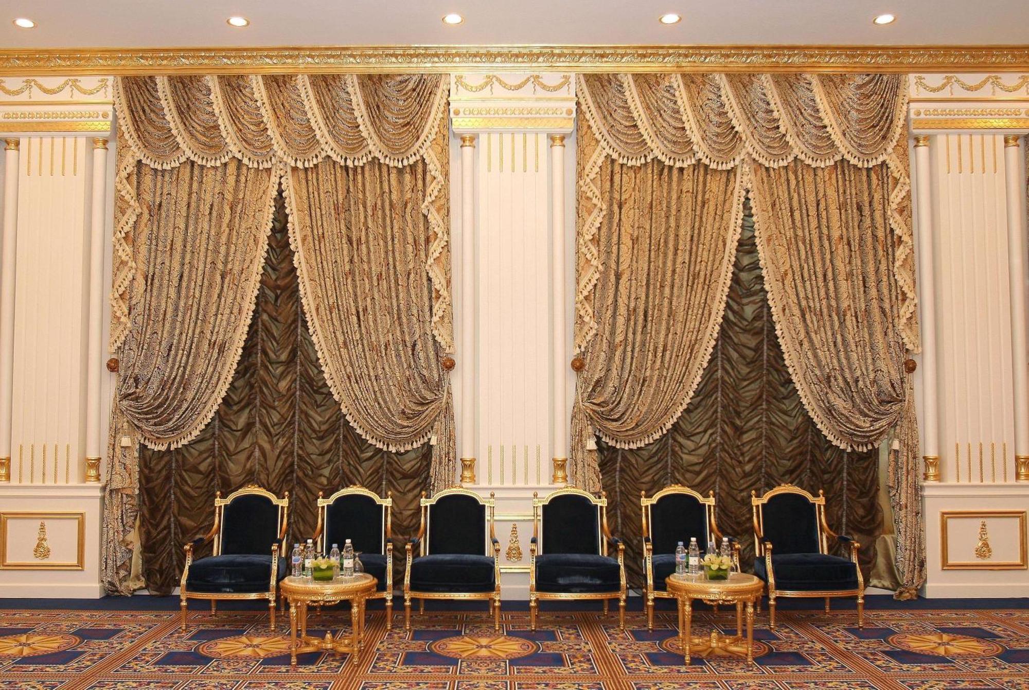 Grand Regency Doha, Trademark Collection By Wyndham Экстерьер фото The photo shows an elegantly decorated interior space. There are two sets of opulent curtains on the walls, featuring rich fabrics with ornate designs and gold accents. The curtains are paired with decorative tiebacks. In front of the curtains, there