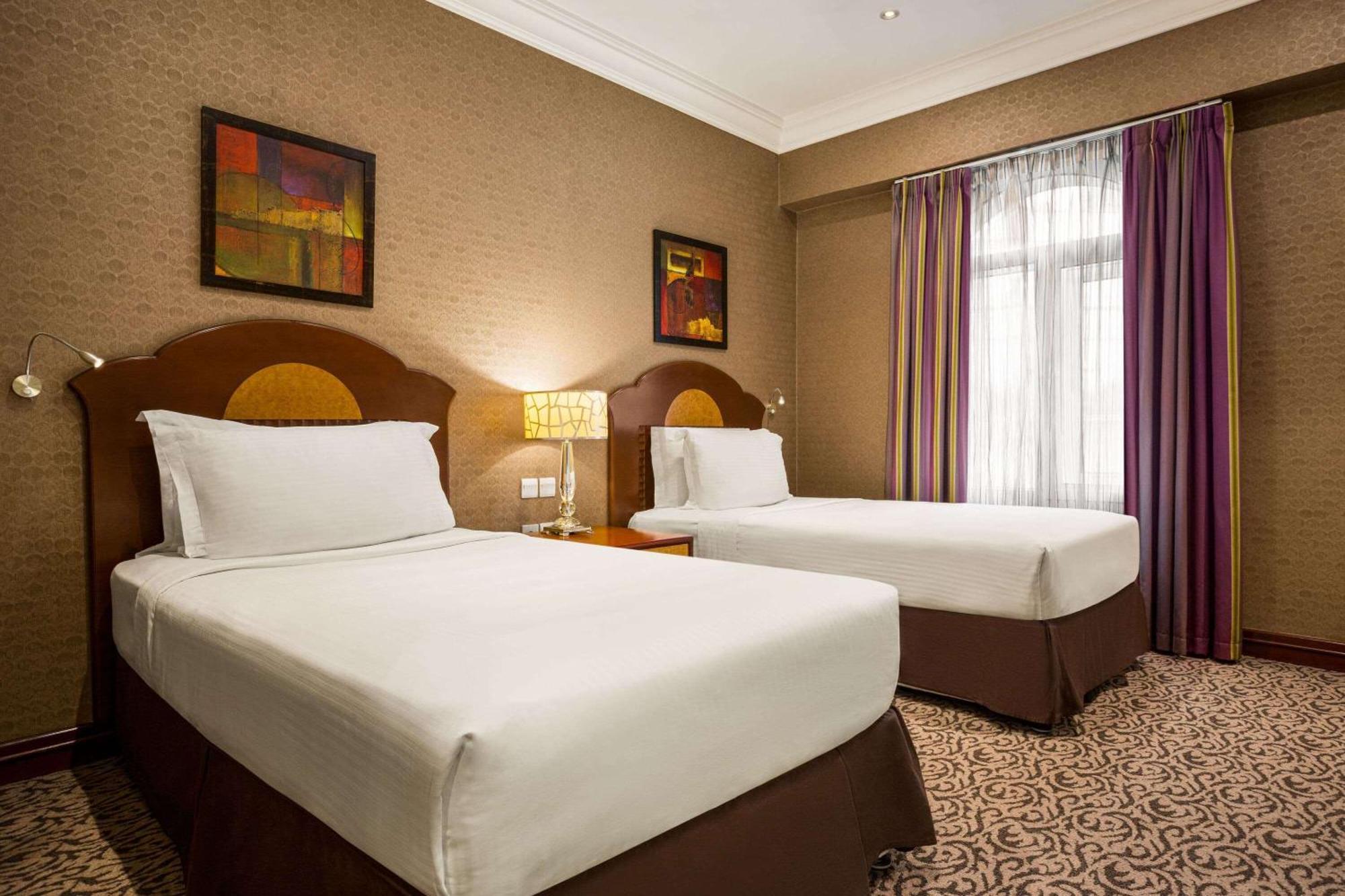 Grand Regency Doha, Trademark Collection By Wyndham Экстерьер фото The photo shows a hotel room featuring two single beds with white bedding and dark brown upholstered headboards. There is a bedside table with a lamp between the beds. On the walls are two abstract paintings, and large windows dressed with sheer curt